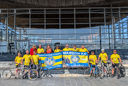 Mae beicwyr o Ganolfan Ieuenctid Margam, Inclusion Stags, yn sefyll ar risiau'r Senedd yn eu dillad beicio, gyda'u beiciau ac yn dal baner eu tîm pêl-droed. Yn sefyll gyda nhw mae Sioned Williams MS a Helen Antoniazzi o Gymdeithas Bêl-droed Cymru.