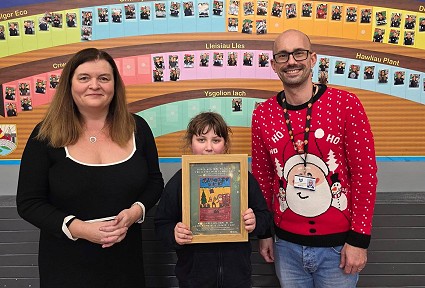 Mae Sioned Williams yn sefyll gyda Seren, a'i hathrawes. Mae Seren yn dal ffrâm gyda chopi o'i dyluniad buddugol ynddi. Y tu ôl iddyn nhw mae wal arddangos gyda'r geiriau 