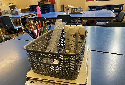 basket on a school desk containing rulers and glue stick