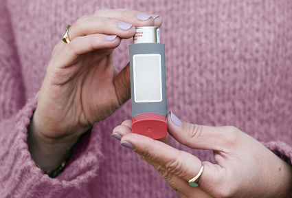 woman in a pink jumper holding a grey inhaler