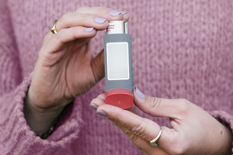 woman in a pink jumper holding a grey inhaler