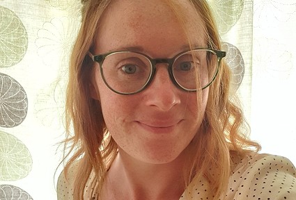 dynes â sbectol yn gwisgo ffrog wen gyda dotiau du yn gwenu am lun