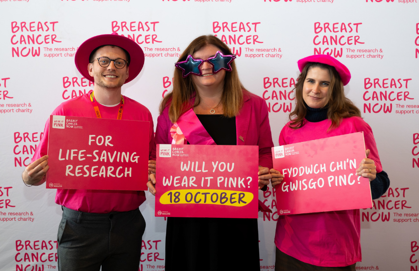Three woman stood together, one holding a plant pot and the other two with posters