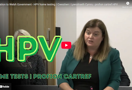 Sioned Williams speaks during a formal session with the large green text 'HPV Home Tests' displayed on the screen