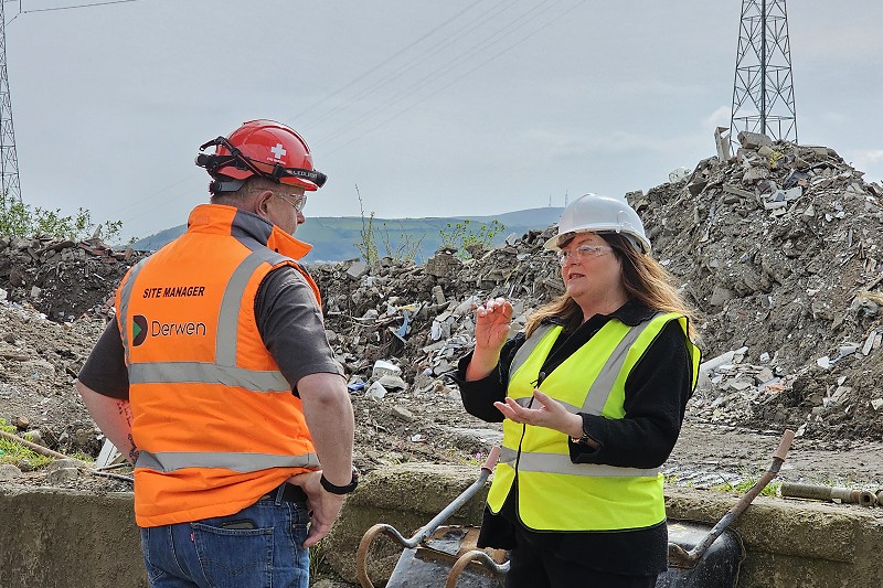 Sioned a dyn mewn siacedi llachar a hetiau caled yn siarad o flaen pentwr mawr o sbwriel yn y ffatri ailgylchu
