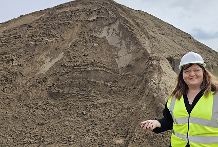 Sioned next to a large pile of sand wearing a hi-viz jacket and a hard hat