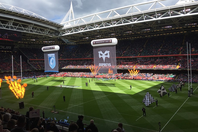 Cae rygbi gyda baneri mawr y Gweilch a'r Gleision yn hongian uwchben