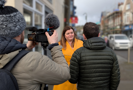 Mae Sioned Williams SM yn sefyll ar stryd fawr Pontardawe, gyda Banc Lloyds yn un o'r siopau y tu ôl iddi. Mae hi'n cael ei chyfweld ar gyfer y teledu a gallwch weld cefnau'r cyfwelydd a'r camerawr wrth iddyn nhw sefyll yn ei ffilmio