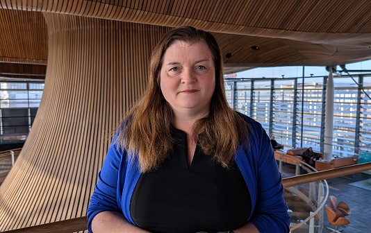 Sioned yn siaced glas atriwm y Senedd