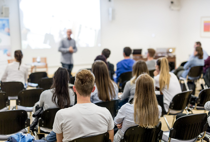 Room full of people looking at a lecture stood in the front of the room