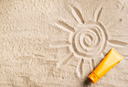 A photograph of a tube of sunscreen lying on sand, onto which a picture of a sun has been drawn