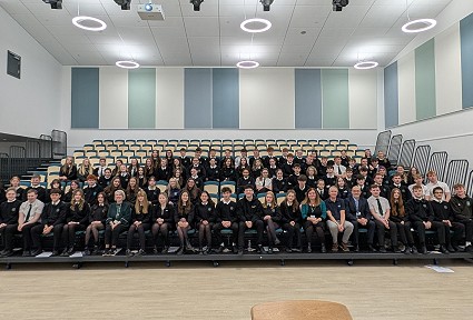 Sioned yn eistedd ymhlith y disgyblion mewn awditoriwm