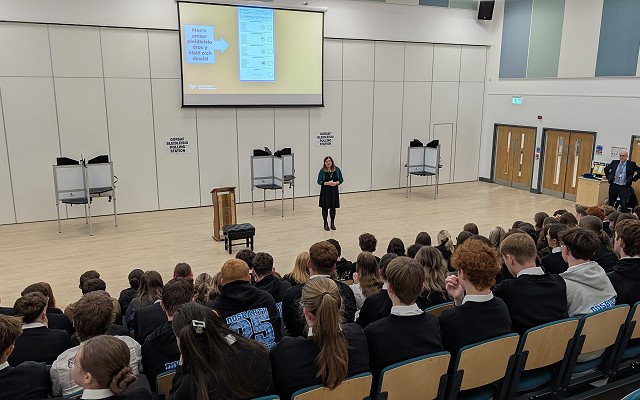 Sioned speaking to pupils in an auditorium