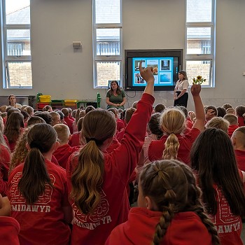 Sioned yn eistedd ac yn siarad â disgyblion ysgol mewn gwasanaeth