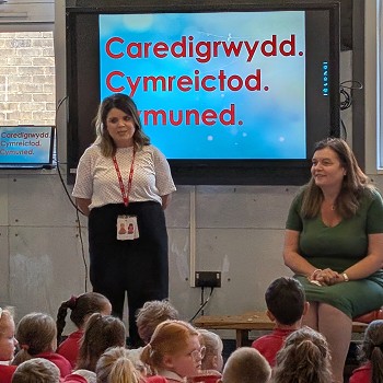Sioned yn eistedd ac yn siarad â disgyblion ysgol mewn gwasanaeth