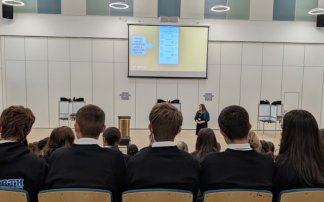 Sioned speaking to pupils in an auditorium